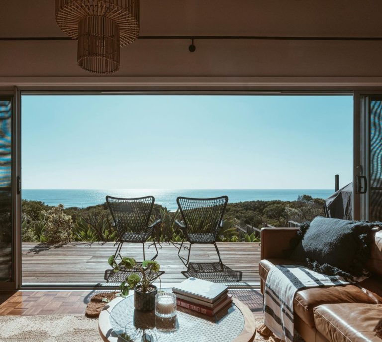 Vue sur la mer depuis un intérieur stylisé avec chaises et plantes.