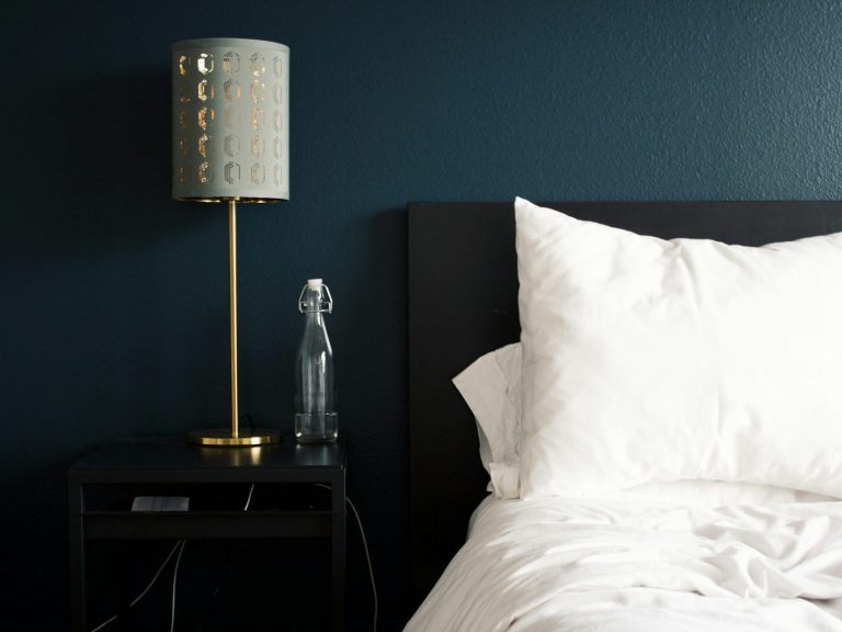 Lit de chambre avec oreillers blancs et lampe décorative sur table de nuit.